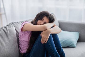 unhappy teen girl feeling depressed or desperate, sitting on couch at home, suffering from problem o