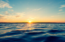 Water Surface. View Of A Sunset Sky Background. Dramatic Gold Sunset Sky With Evening Sky Clouds Over The Sea. View Of A Crystal Clear Sea Water Texture. Landscape. Small Waves. Water Reflection
