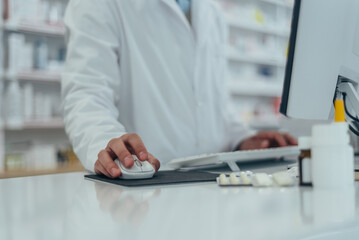 Close shot of pharmacist working in a pharmacy while using a computer