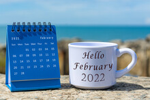 Hello February 2022 Written On White Coffee Cup With Blue Calendar