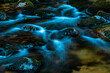 Blue hour, a photo of a mountain stream in the Carpathian Mountains in Poland. Stones covered with green lichen and ice. Shiny beautiful green and blue. The flowing water turns white and blue. 