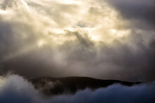 雲から漏れる日光と霧が広がるなかの山
