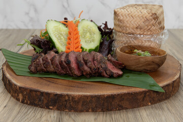 Delicately decorated timber plate of nua yang Thai meal consisting of sliced seasoned steak, basekt of rice, and vegetable salad