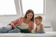 © Friends Stock - Smiling mother reading a book the baby in bed