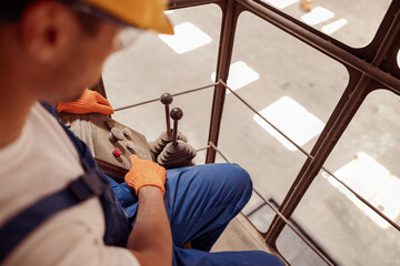 Male worker operating industrial overhead crane at factory