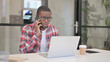 © stockbakers - Angry African Man Talking on Smartphone while using Laptop