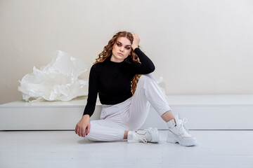 A beautiful woman with long curly hair in a black sweater, white pants, white leather sneakers. New collection of women's casual shoes