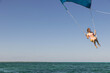 © Mat Hayward - Girl flying over the Caribbean sea during fun activity with a spinnaker parachute ride. The wind is lifting her into the air as she holds on to the kite.