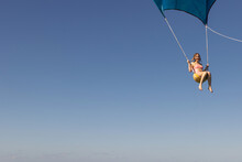 Girl Flying Over The Caribbean Sea During Fun Activity With A Spinnaker Parachute Ride. The Wind Is Lifting Her Into The Air As She Holds On To The Kite.