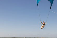 Girl Flying Over The Caribbean Sea During Fun Activity With A Spinnaker Parachute Ride. The Wind Is Lifting Her Into The Air As She Holds On To The Kite.