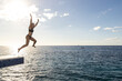 © Mat Hayward - Young woman jumps from diving platform into the ocean water of the Caribbean sea while on a tropical island vacation on Cozumel, Mexico.