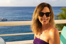 Beautiful Woman Wearing Sunglasses Outside On The Patio With A Stunning View Of The Caribbean Sea Surrounding Cozumel, Mexico In Quintana Roo.