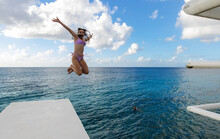 Young woman jumping off diving platform into blue Caribbean sea near coast of tropical island Cozumel, Mexico during vacation.