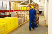 Worker Moving Wooden Pallets With Manual Forklift In Warehouse, Back View
