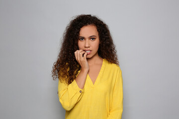 African-American woman biting her nails on grey background