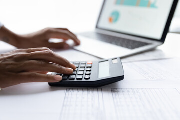 Close up young african american woman using calculator, managing business expenses, making financial audit, reviewing utility bills taxes, planning household monthly budget, accounting in computer app