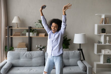 Relaxed Cheerful Young African American Woman Listening Energetic Music In Wireless Headphones From Mobile Application, Dancing Alone In Modern Living Room, Enjoying Carefree Leisure Weekend Time.