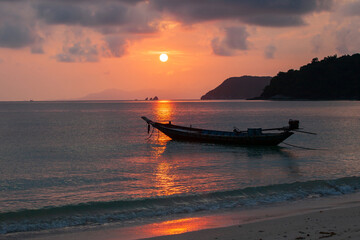 Wall Mural - Tropical beach and a wooden fishing boat at sunset.