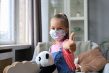 Stay At Home Quarantine Coronavirus Pandemic Prevention. Sad Child In Protective Medical Mask And Her Panda Bear Sit On Rocking Horse, Looking Out The Window.