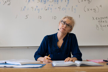 Portrait of frustrated tired high school math teacher sitting on desk talking to students.