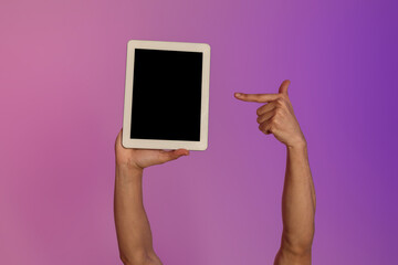 Poster - Cropped view of millennial man pointing at tablet computer with empty black screen in neon light, mockup