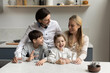 © fizkes - Happy parents and two healthy sibling kids drinking pure fresh clean water in kitchen, satisfying thirst, standing at table with glasses, smiling, laughing. Family care, children healthcare concept