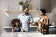 © fizkes - Happy laughing African American family couple and healthy daughter kid drinking clean still pure water in home kitchen, holding glasses, talking, laughing, keeping healthy hydration