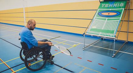 Adult man with a physical disability who uses wheelchair playing tennis on indoor tennis court