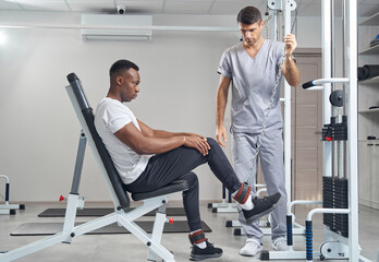 Wall Mural - Focused male patient doing strength training exercise supervised by physiatrist