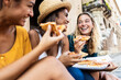 © Xavier Lorenzo - Three young multiracial women laughing while eating a piece of pizza in italian city street - Happy female friends enjoying holidays together in Italy - Friendship, travel and tourism concept