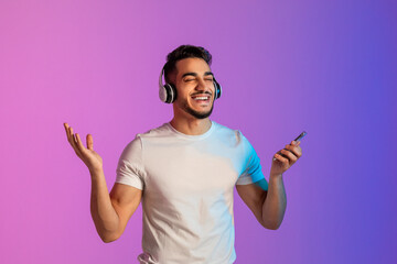 Poster - Cool Arab man listening to popular song in headphones, checking new mobile music app on phone, relaxing in neon light