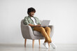 © Prostock-studio - Happy indian guy in casual sitting in armchair with laptop