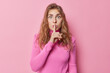 © WHstudio Leushin N - Shocked impressed young European woman stares bugged eyes makes silence gesture asks to be quiet stands mute wears casual turtleneck isolated over pink background. Hush do not make any sound
