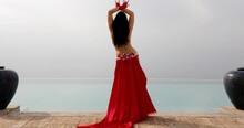 A Beautiful Belly Dancer In A Red Costume Performing Front Of The Pool And Open Sea, Smoothly Moving Showing Curves Of The Waist In Motion - Back View 