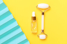 Bottle With Dropper Of Aroma Essential Oil. Face Roller On Yellow Background And Blue Fan. Creative Trendy Cosmetics Flat Lay With Copy Space