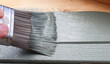 A close up of a decorator's paint brush being used to paint wood a smokey green colour 