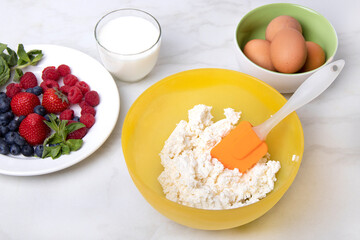 Cottage cheese in a yellow bowl on the table among fruits and eggs