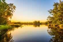 Sunset Over The River. Clear Sky. Overgrown Coastline. Smooth Surface Of Water. Russia, Europe.