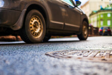 Rainy Day In The City. A Car Drives By Along The Road. Rainy Day In The City. The Road After The Rain. Focus On The Manhole Cover. Close Up View Of A Manhole Cover At The Level Of The Asphalt.