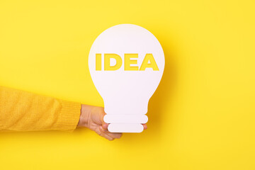 Wall Mural - idea inscription on white light bulb, light bulb in hand  over yellow background