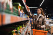 © Andrii  - Happy young woman looking at product at grocery shop. Customer buying food at the supermarket