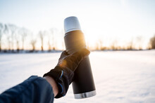 Steel Vacuum Thermos Hold In Your Hand In Nature. Black Thermos With Metal Cup. Hot Tea In Nature In The Rays Of The Setting Sun.