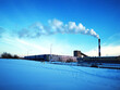 A wide view of an industrial complex with a tall pipe with smoke