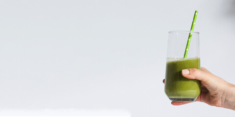 A woman's hand holds a glass with green smoothies on a white background. Banner.