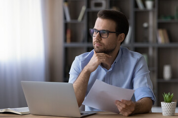 Poster - Thoughtful serious businessman in glasses touching chin, looking in distance, planning, holding document, sitting at desk with laptop, pensive man thinking, accountant working on financial report