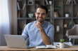 © fizkes - Head shot portrait of smiling successful businessman sitting at workplace desk with laptop, happy young man freelancer or student looking at camera, working or studying online, home office