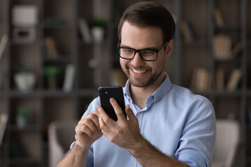 Head shot smiling man wearing glasses using smartphone, chatting online in social network with friends, typing, looking at screen, friendly businessman entrepreneur browsing mobile device apps