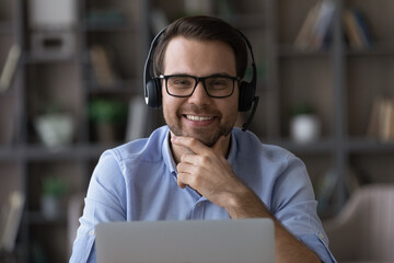 Wall Mural - head shot portrait smiling man call center operator in glasses looking at camera, using laptop, prof