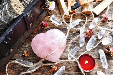 Wall Mural - A top view image of a heart shaped rose quartz crystal with a lit candle and dried rose buds on a dark wooden table. 