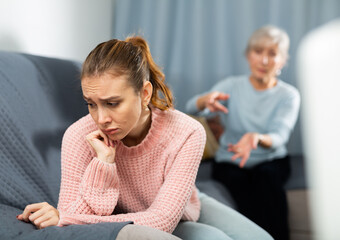 Wall Mural - Young woman sitting on sofa and feeling sad. Her grandmother sitting beside and trying to comfort her.